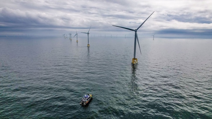An aerial shot shows a distant ship moving toward an offshore wind farm.