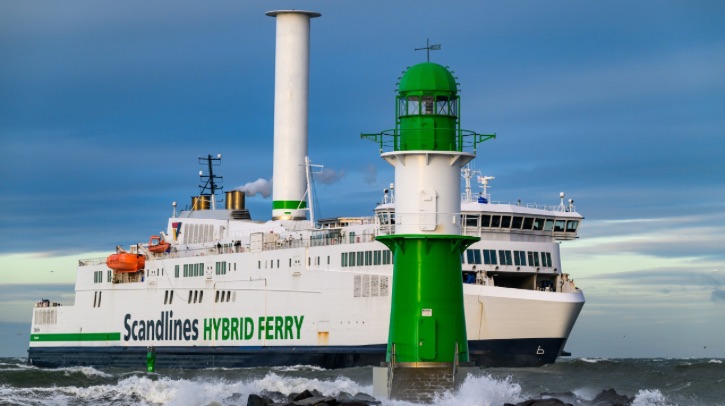 A Scandlines hybrid ferry moves past a green light house.
