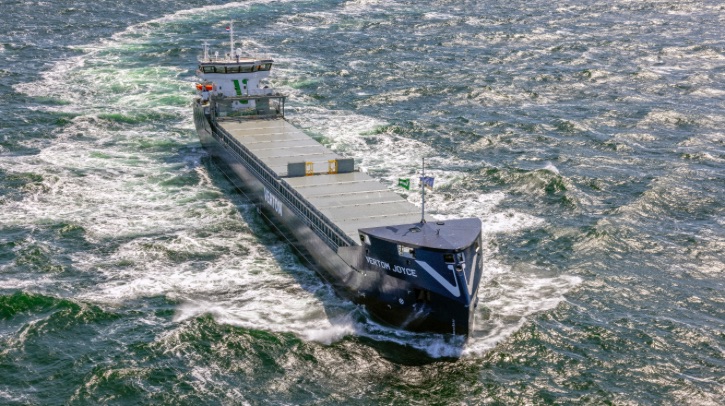 The image shows an overhead view of a large blue dry cargo vessel moving through the ocean