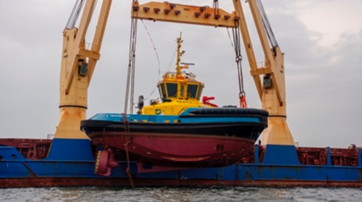 A yellow, blue and red electric tug is lowered into the water.