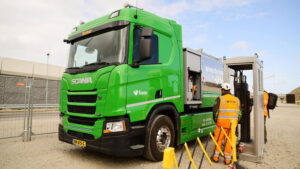 A man in high-vis stands next to a bright green HGV.