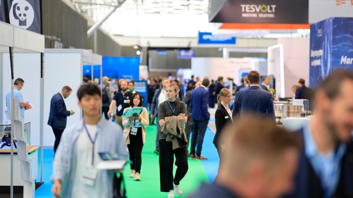 A blonde woman walks down a busy expo hall.