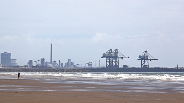 Dog walkers roam the Aberavon Beach as Port Talbot looms in the distance
