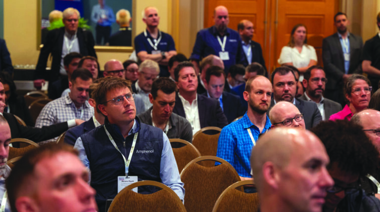 A packed conference room with people sitting n rows listening to a speaker
