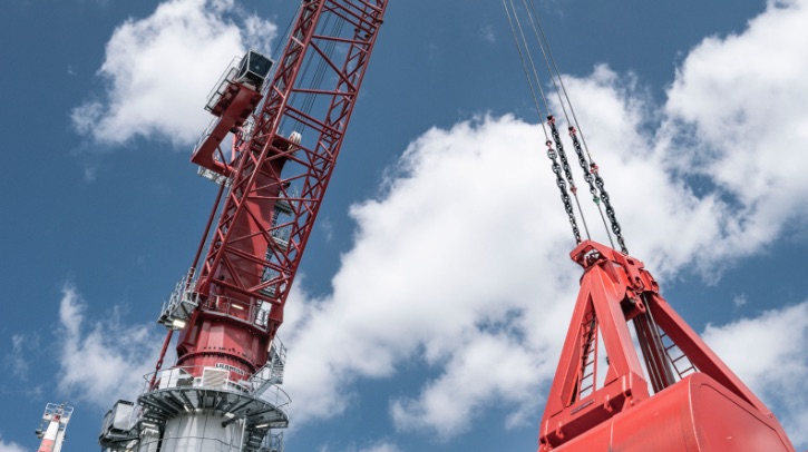 A red crane lifts a piece of cargo against a blue sky.