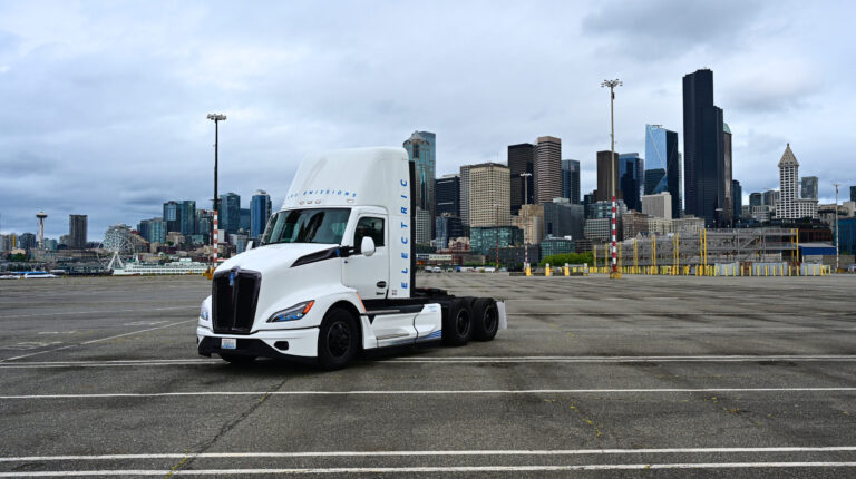 A zero-emission truck tractor for Northwest Seaport Alliance is parked at the Port of Seattle, with a cloudy sky above.
