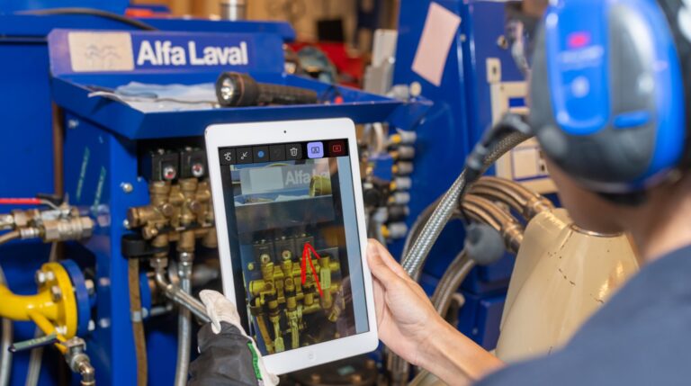 Close up of an engineer wearing ear defenders and using AR-enabled remote support on a tablet to boost vessel performance and compliance.