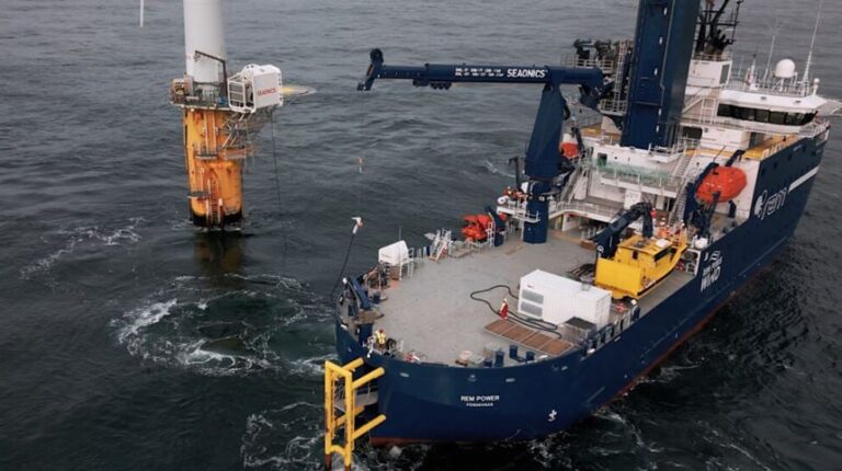 An electric boat uses a test version of the new magnetic plug system that enables offshore charging of electric vessels. The boat has a blue hill and the water is a dark grey.