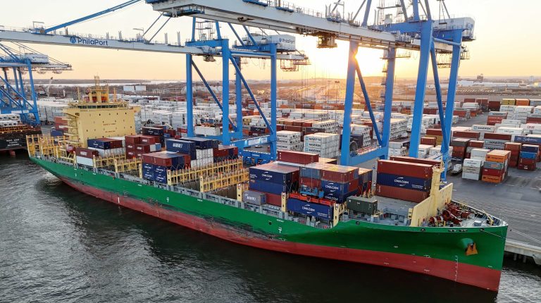 European consortium launches €4m project to accelerate maritime retrofits A large tanker ship with a green hull at a port with cranes and rows of containers stacked on the docks.